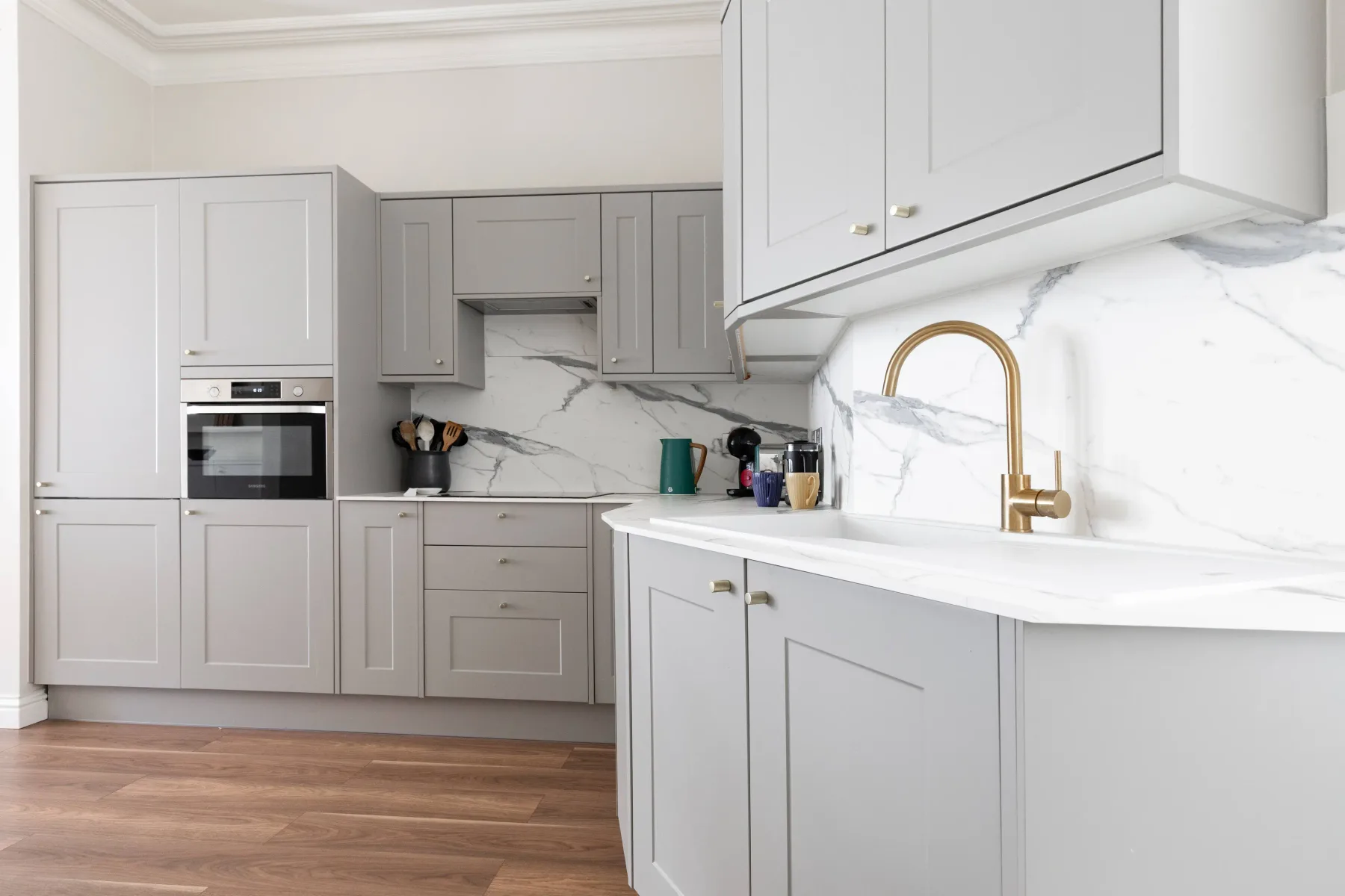 A bright kitchen with gray cabinetry, a white countertop, and a gold faucet.