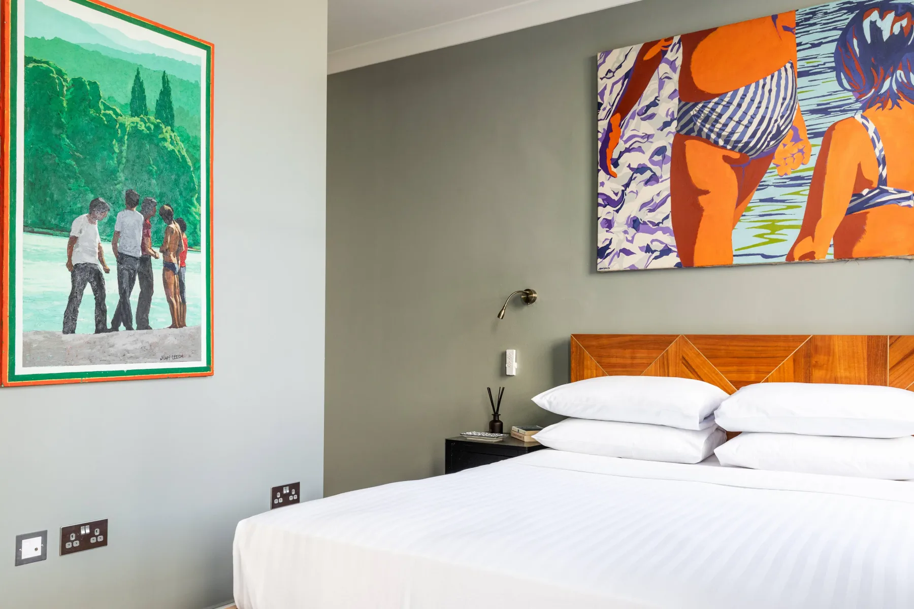 A bedroom with a neatly made bed beneath colorful wall art.