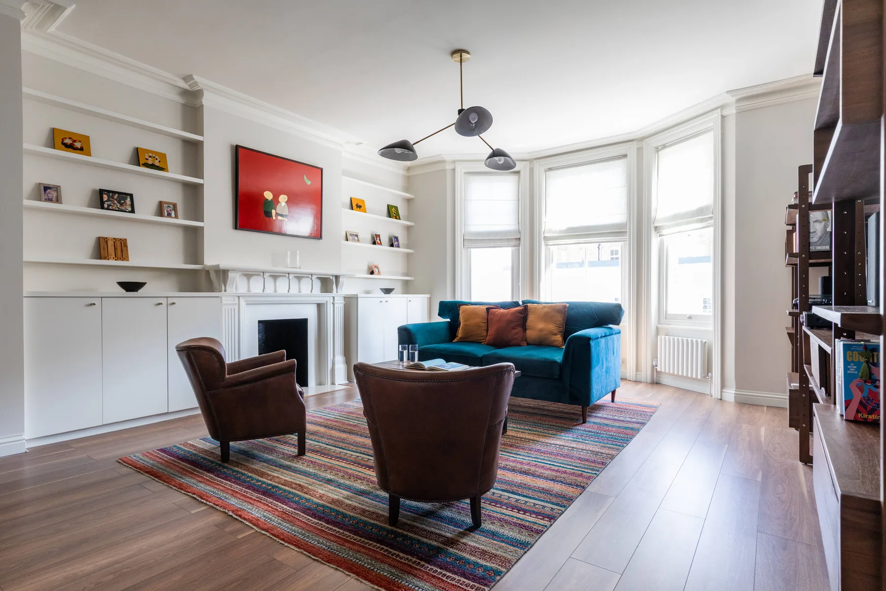 A bright living room with a blue sofa and two armchairs around a striped rug.