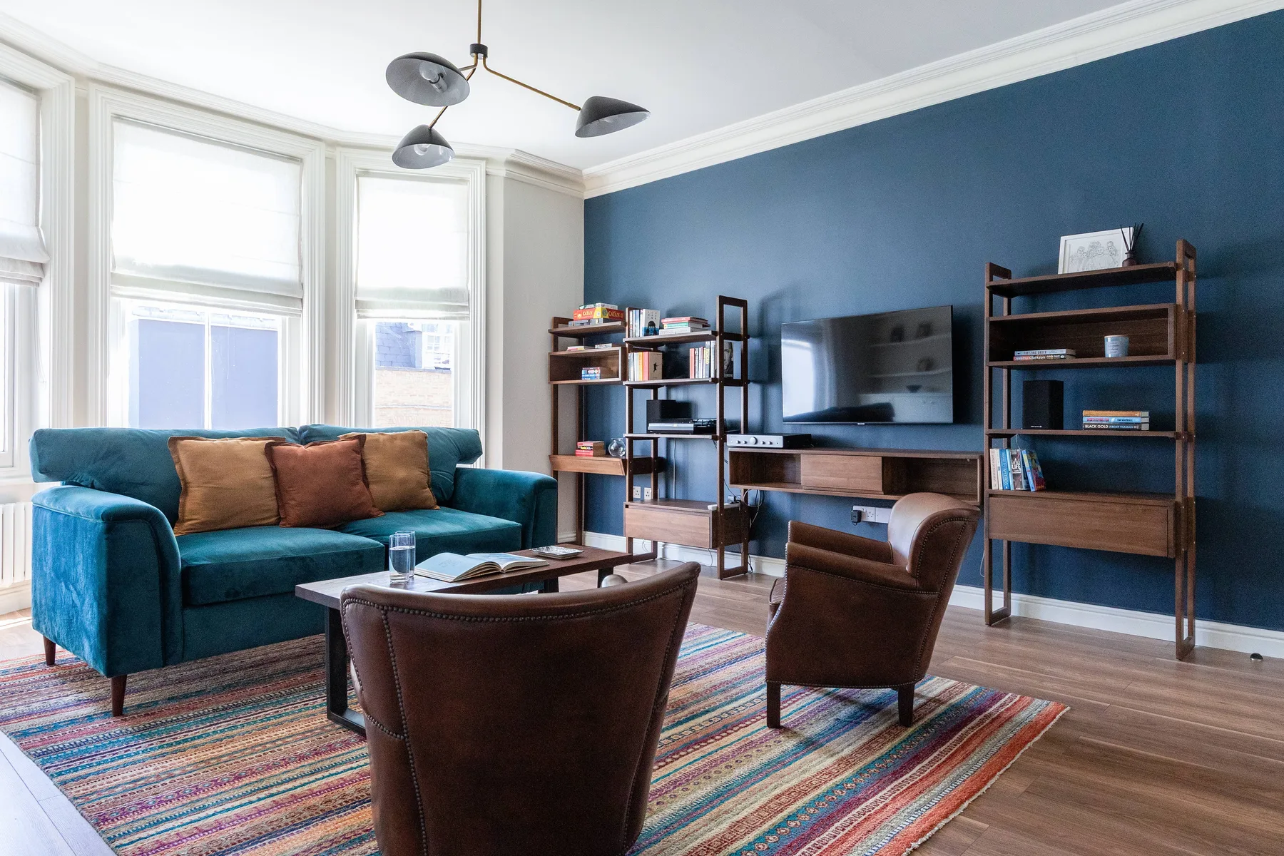 Living room with teal seating, a television, and a colorful striped rug.