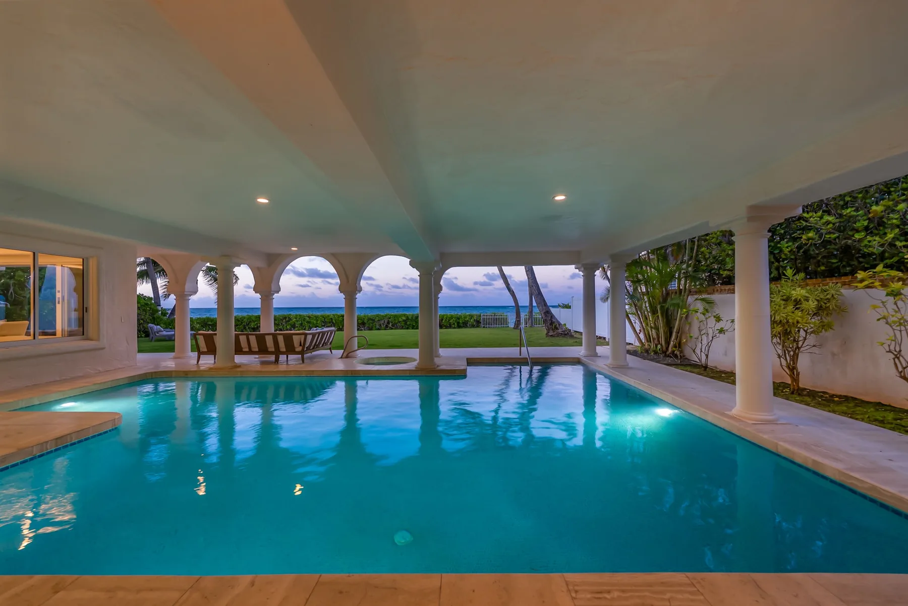Una piscina cubierta se abre a un patio con arcos y jardín.
