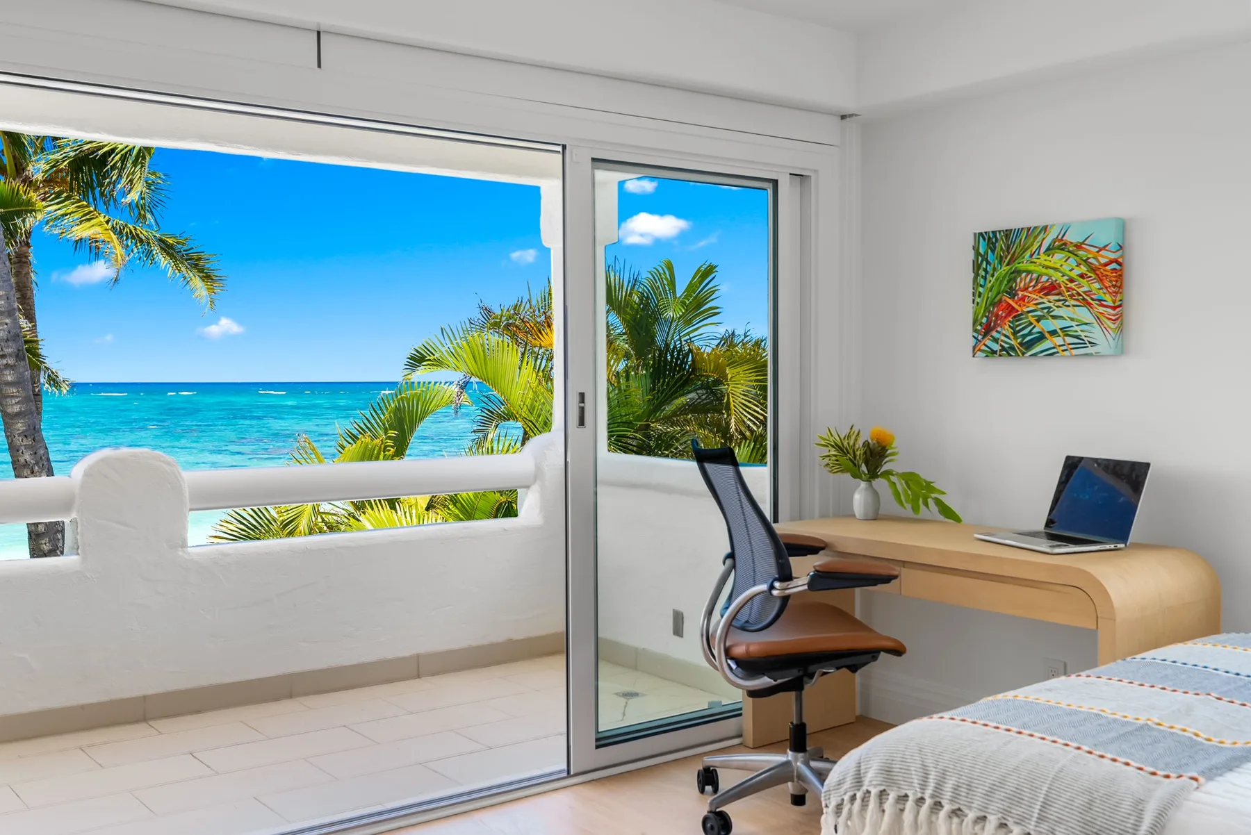 Un espacio de trabajo en un dormitorio junto a una puerta de vidrio, con cama y vista al mar.