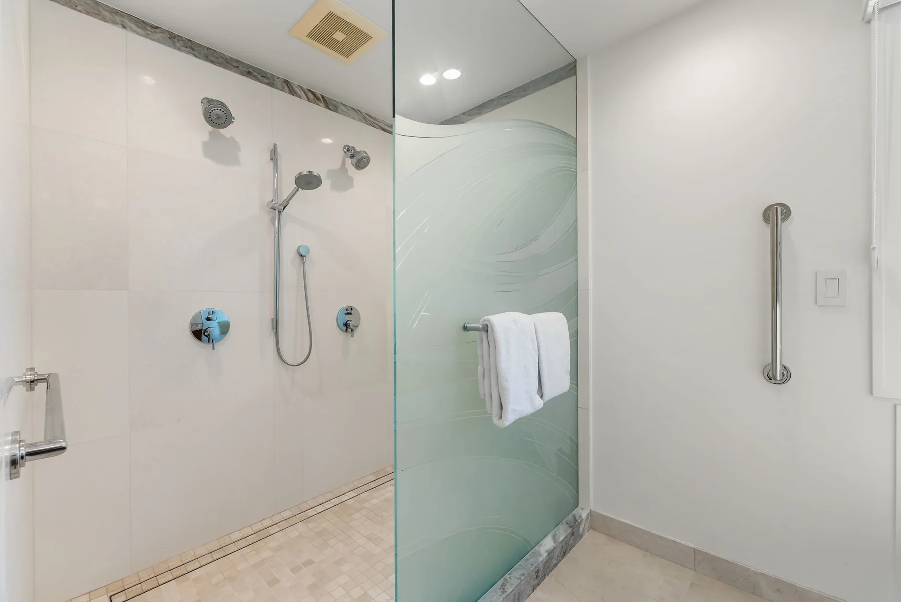 Una ducha de baño con azulejos, un panel de vidrio y una toalla colgada cerca.