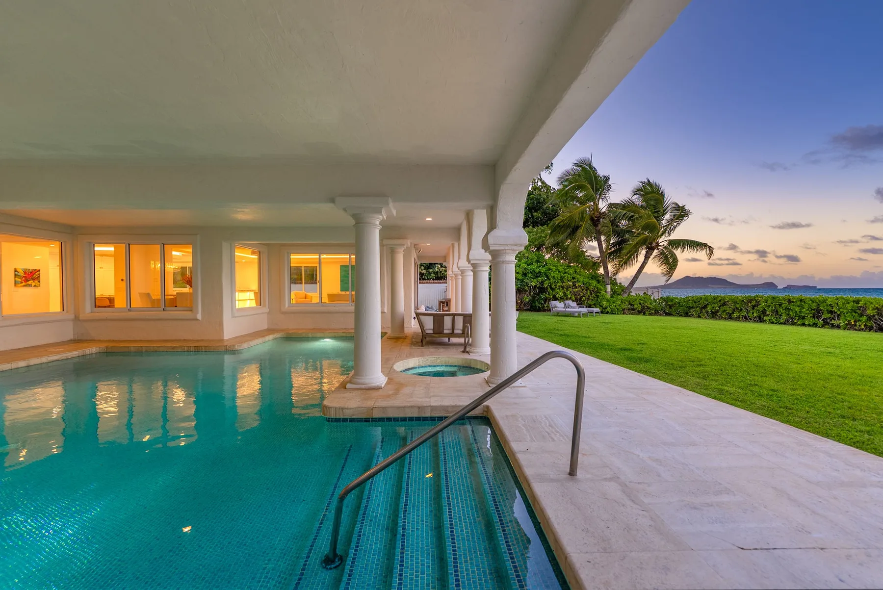 Una piscina cubierta se abre a un césped y un jardín tropical al atardecer.
