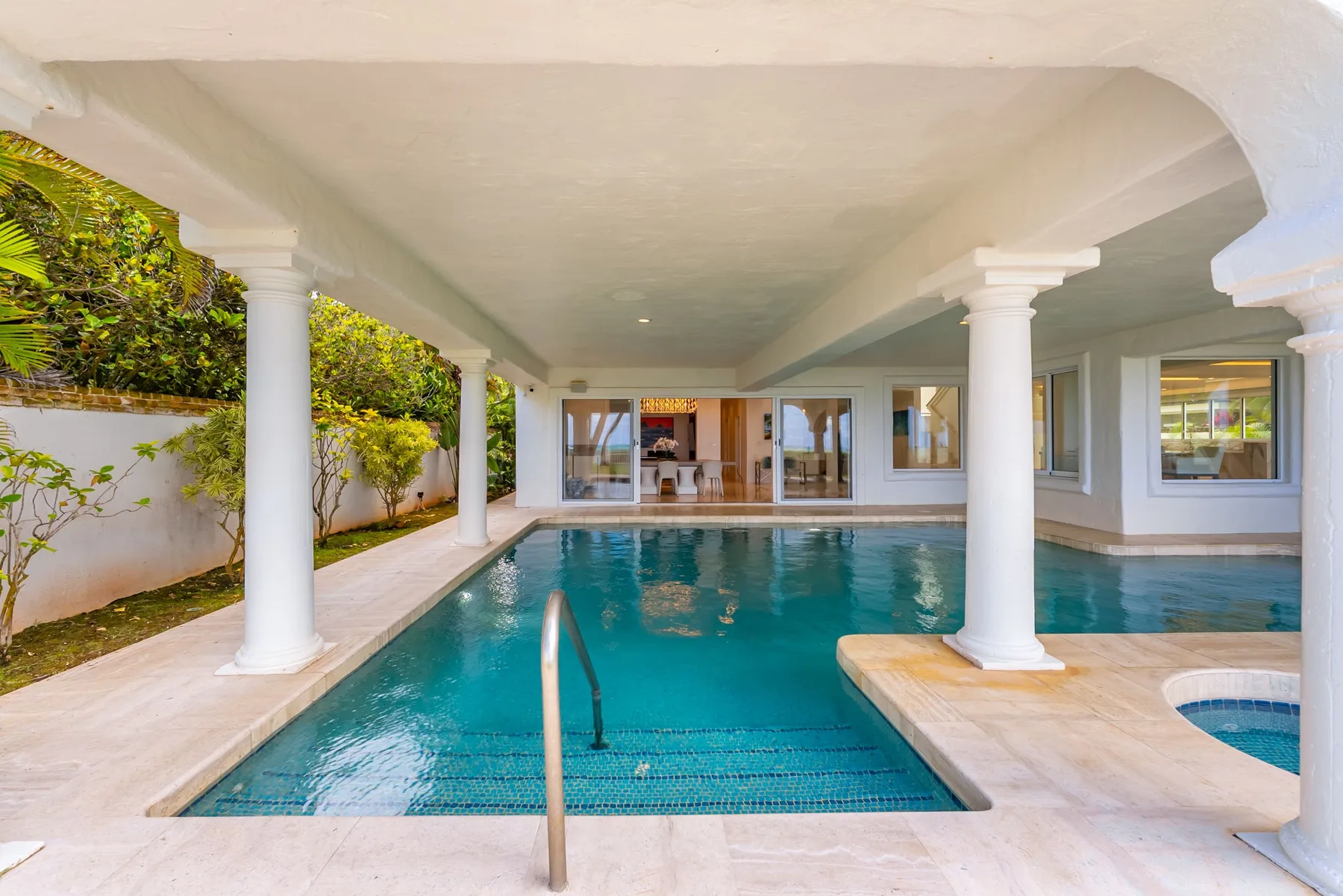 Una piscina cubierta junto a un edificio, con columnas blancas y ventanas.
