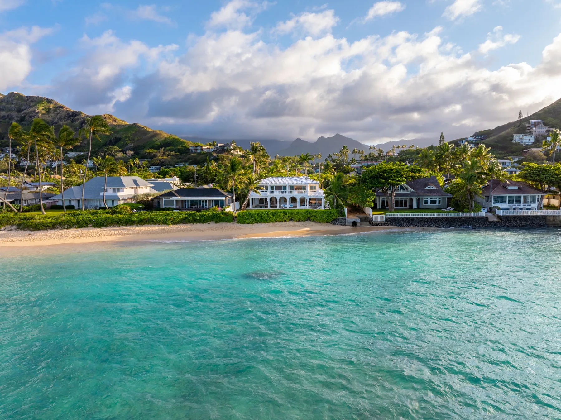Una costa tropical con aguas turquesas claras, una playa de arena y casas junto al mar.