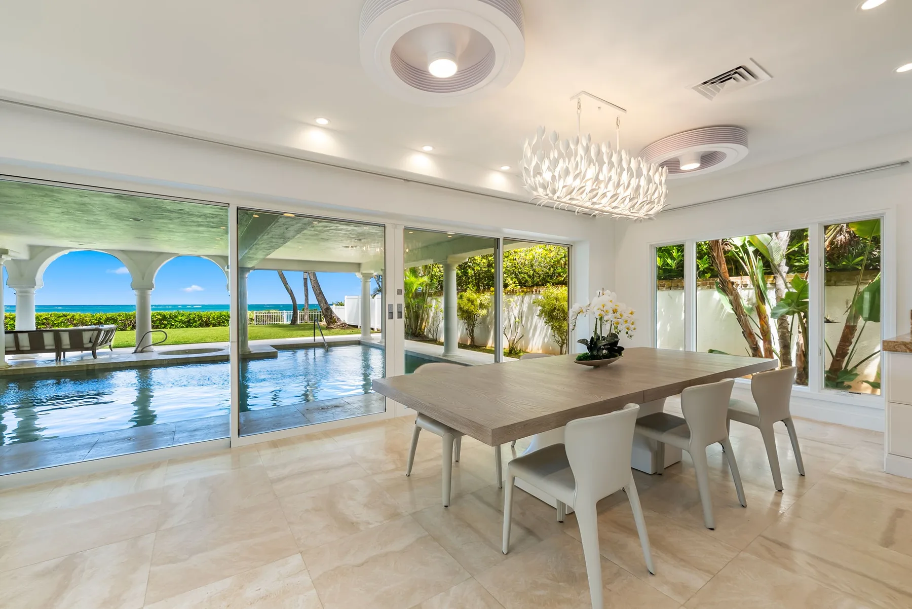 Un comedor luminoso con una mesa larga y ventanas con vistas a una piscina.