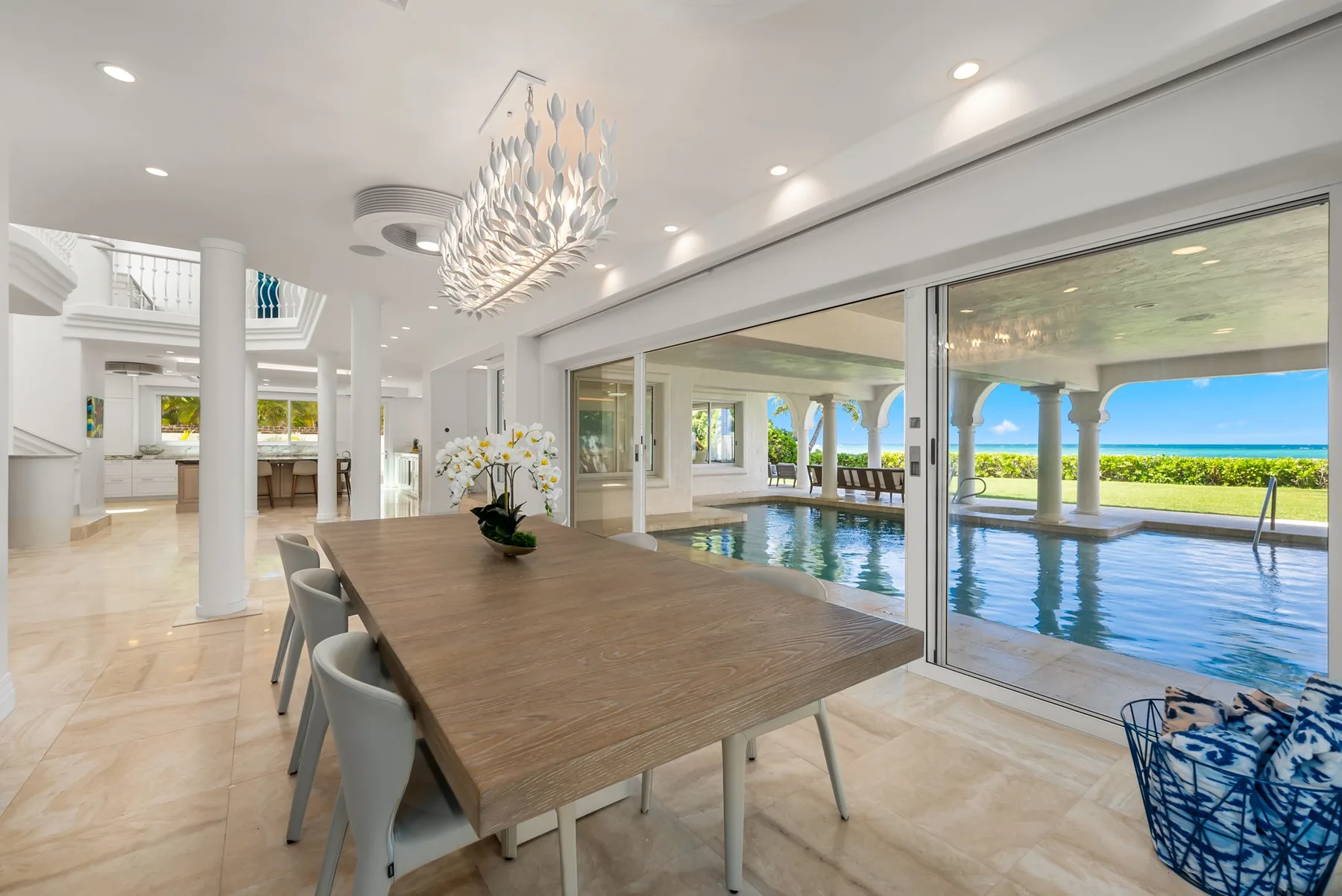 Un comedor luminoso da a una piscina y ofrece vistas al mar a través de puertas corredizas de vidrio.