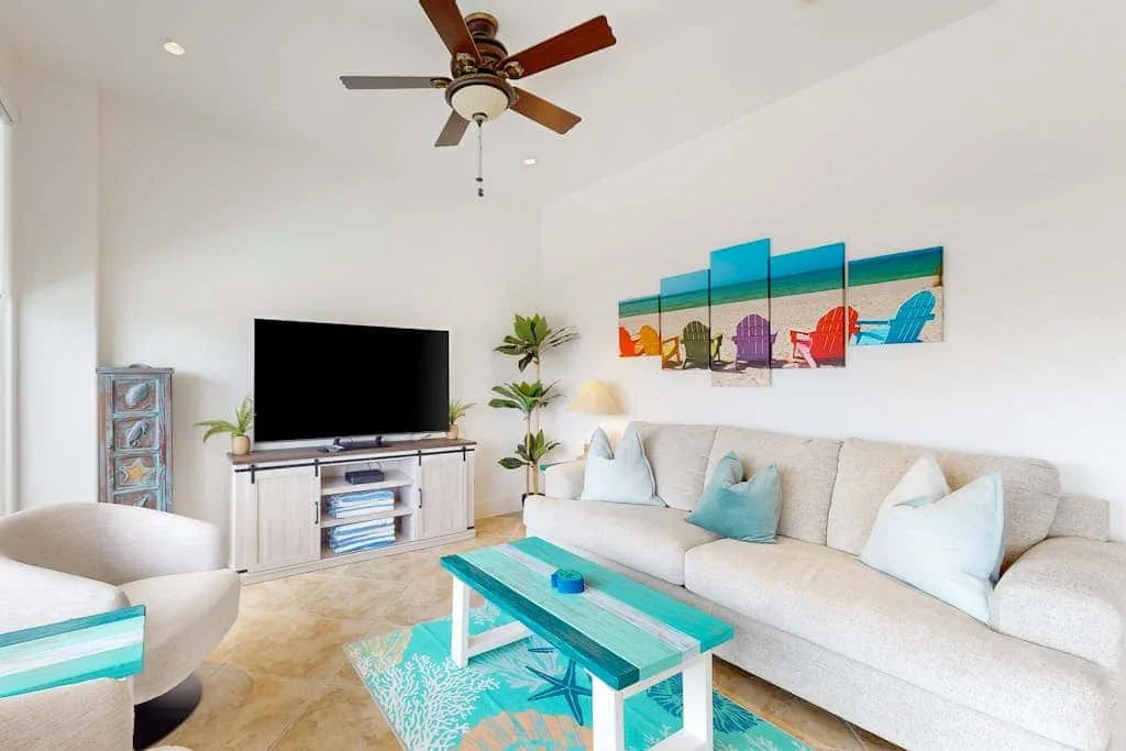 A bright living room with a long sofa, coffee table, and wall-mounted artwork.