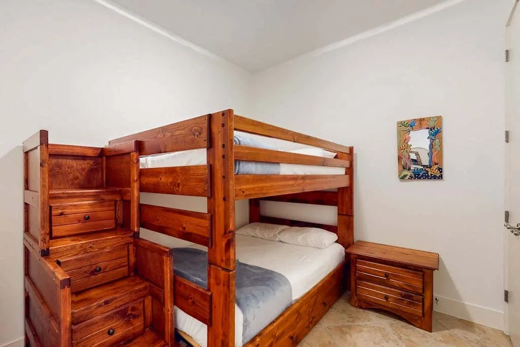 A bedroom with a wooden bunk bed, built-in drawers, and a small bedside cabinet.