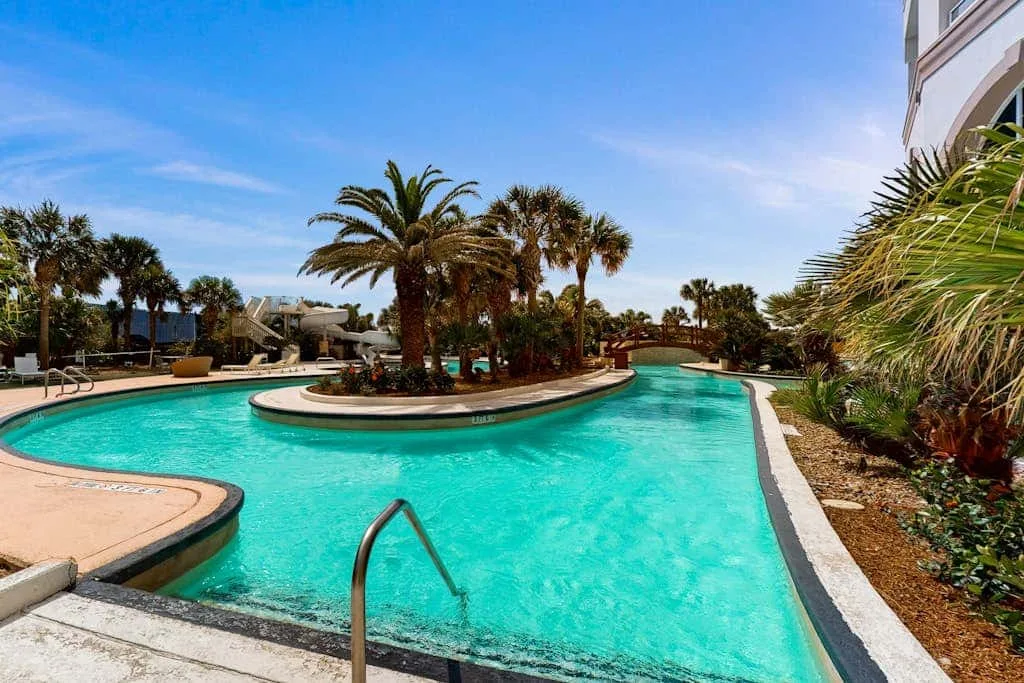 A turquoise outdoor pool curves around a landscaped island of palm trees.