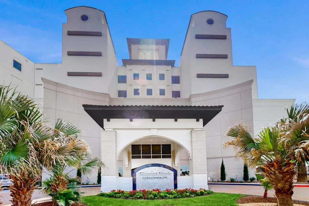 A white multi-story building stands behind a covered entrance and landscaped grounds.
