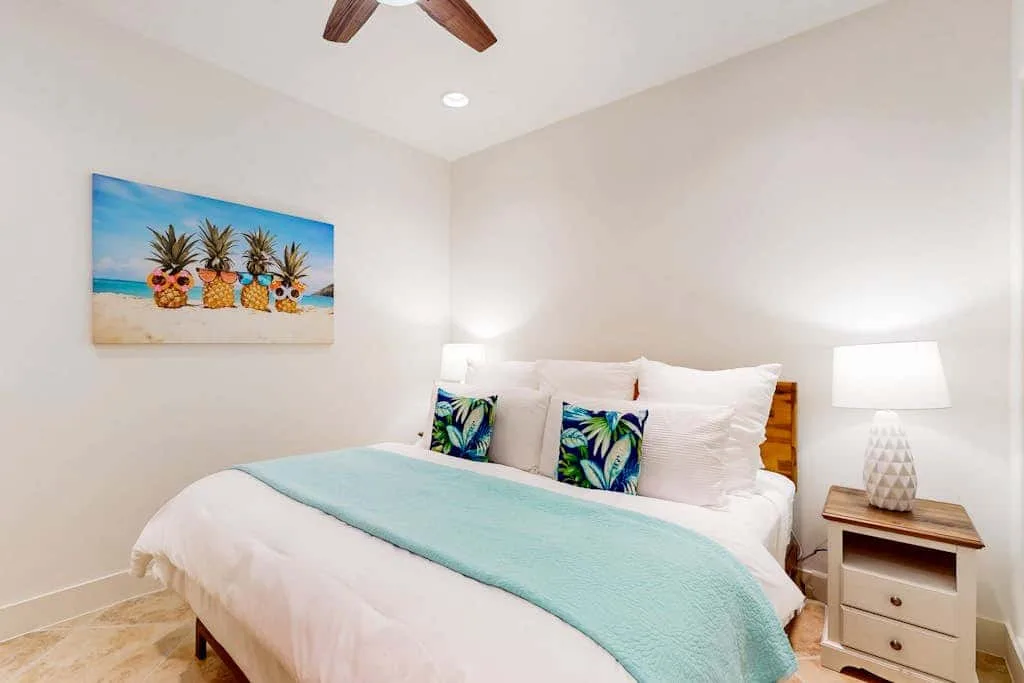 A bedroom with a neatly made bed, pale blue cover, and colorful wall art.
