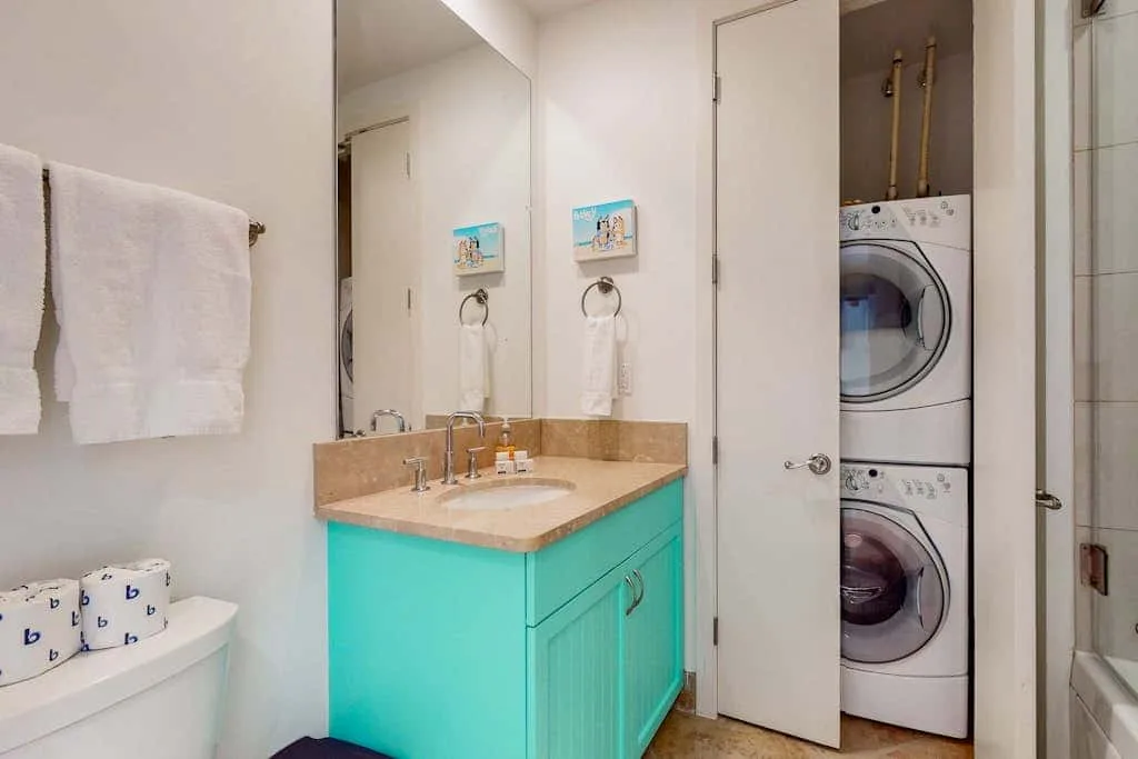 A bathroom vanity with a turquoise cabinet stands beside a stacked washer and dryer.