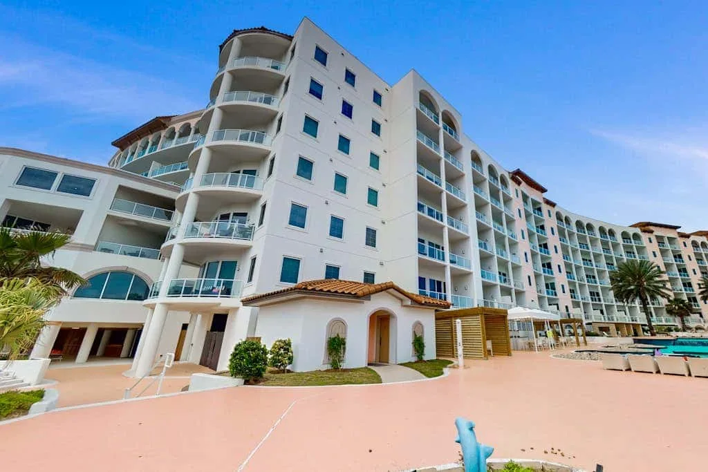 A large white multi-story building with balconies stands beside a paved courtyard.
