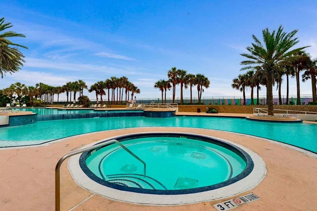 A swimming pool with a circular spa in the foreground and palm trees beyond.