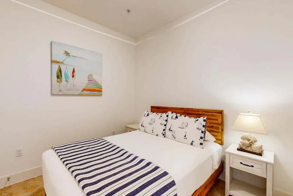 A bedroom with a bed, striped blanket, and bedside table.