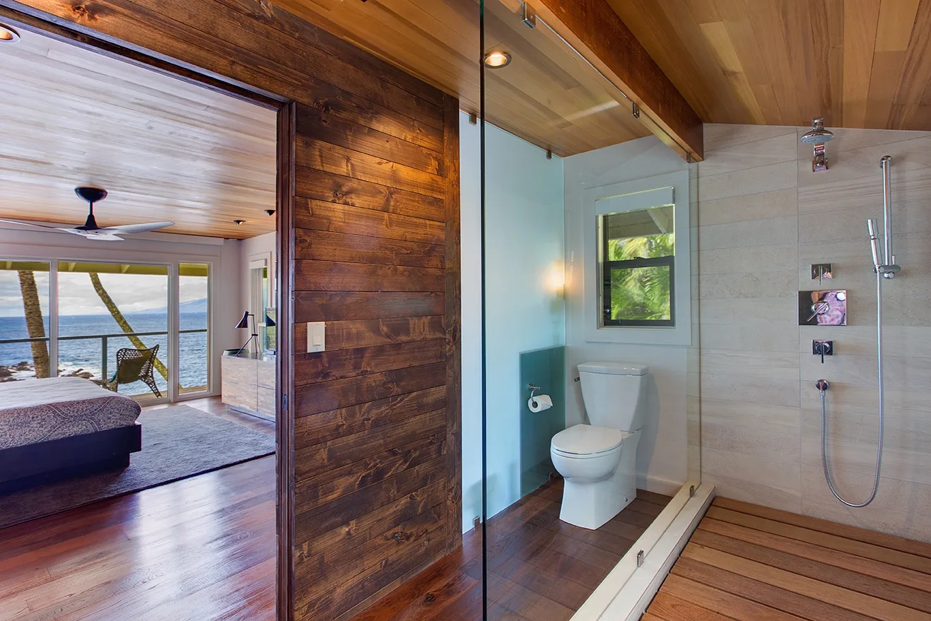 Un baño con inodoro y ducha junto a un dormitorio con vistas al agua.