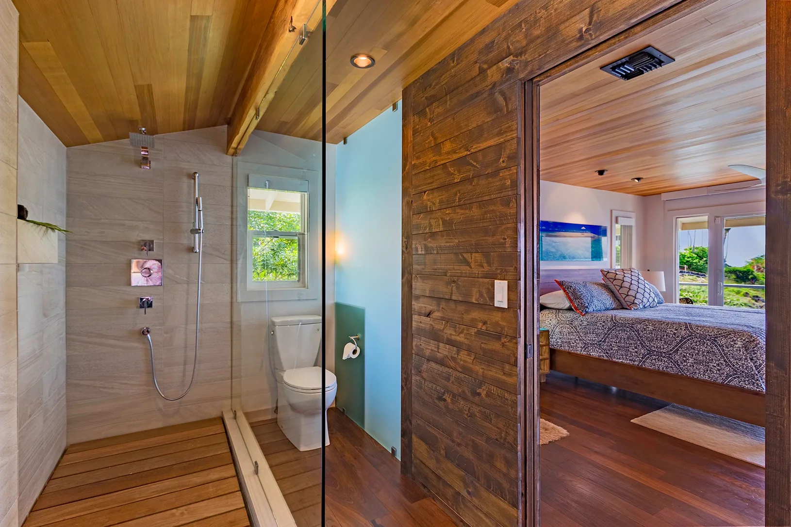 Un dormitorio y un baño contiguo comparten techos revestidos de madera y acabados cálidos.