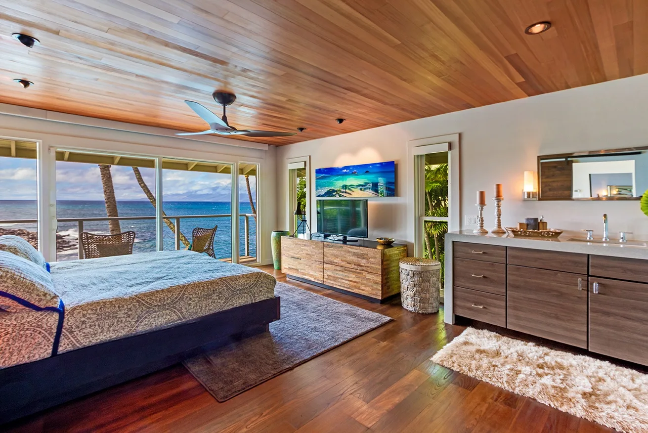 Un dormitorio con una cama frente a un televisor y puertas corredizas de vidrio con vista al mar.