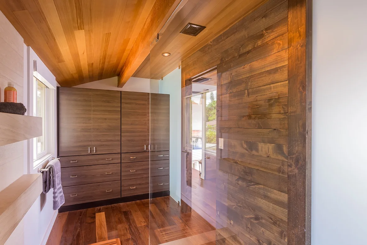 Un vestidor revestido de madera con armarios empotrados y una ducha de vidrio.