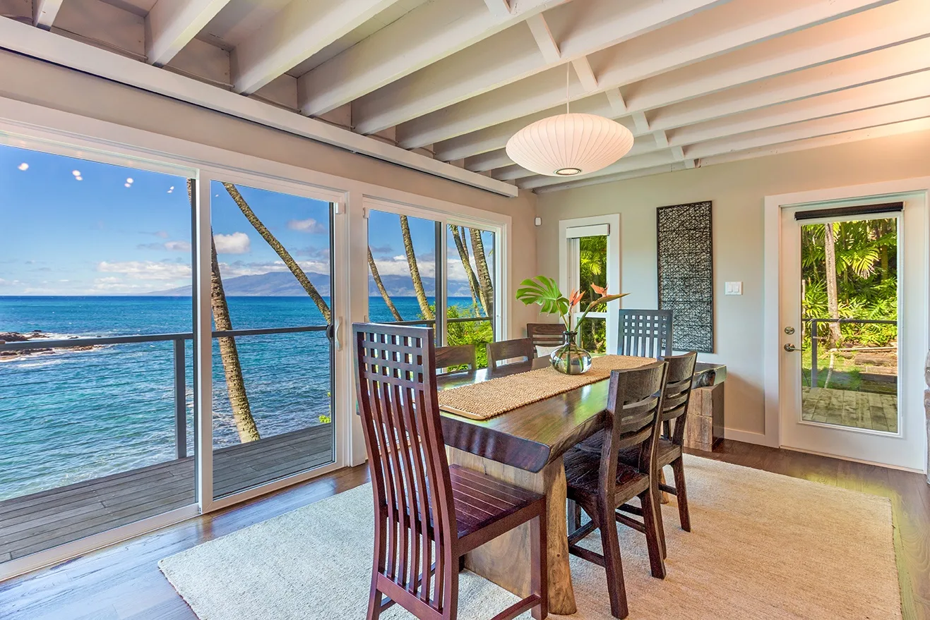 Un comedor con una mesa de madera junto a grandes ventanas con vista al océano.