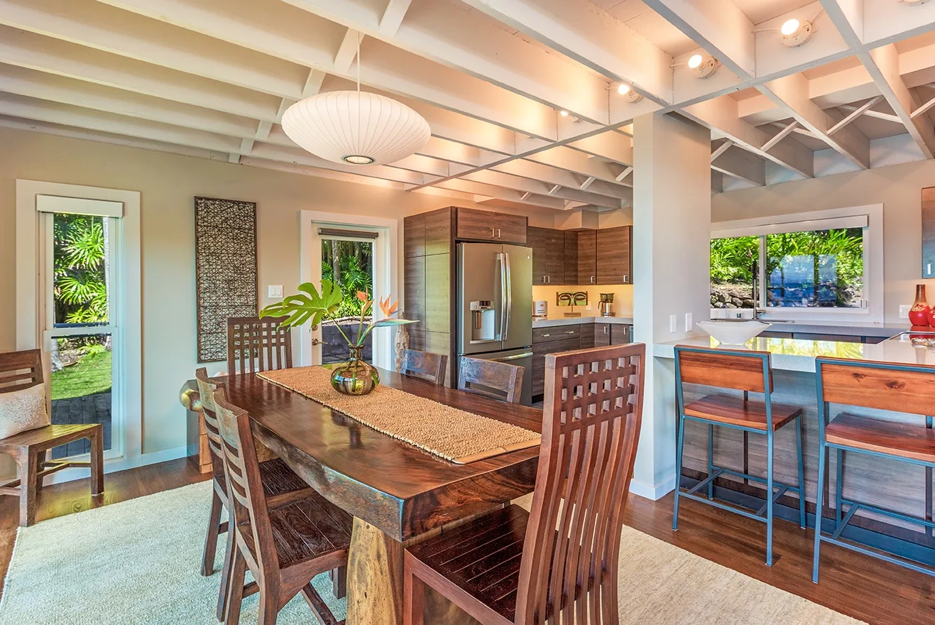 Comedor con mesa de madera junto a una cocina abierta y asientos en la barra.