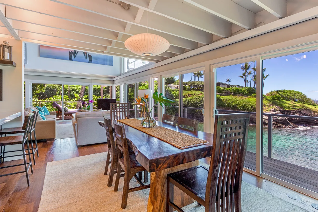Un comedor luminoso con una mesa de madera junto a grandes ventanales con vistas al agua.