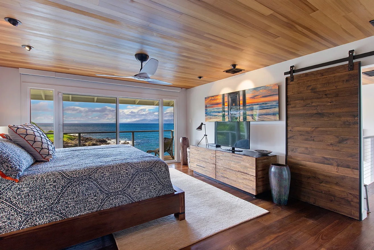 Un dormitorio con una cama grande, un televisor y amplias ventanas con vista al mar.