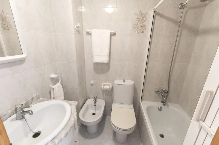 A tiled bathroom with a sink, toilet, bidet, and bathtub with shower.