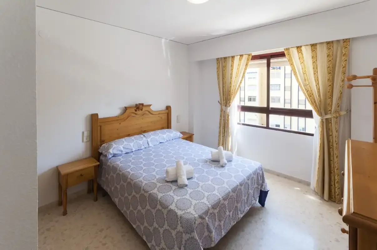A bedroom with a double bed and a window framed by patterned curtains.