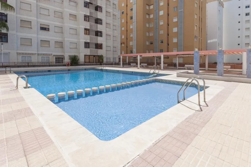 An outdoor swimming pool with blue water sits among surrounding apartment buildings.