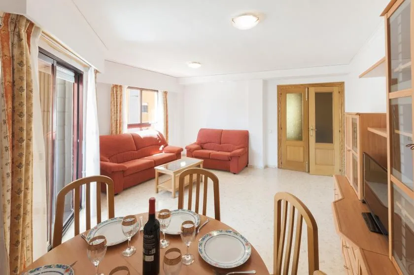A bright living room with red seating, a dining table, and wooden cabinets.