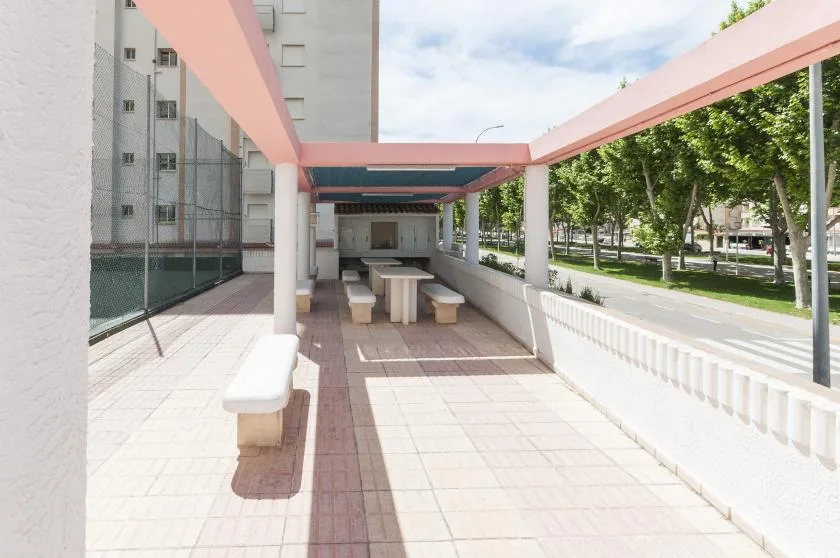 A covered outdoor seating area with tables and benches overlooks a tree-lined street.