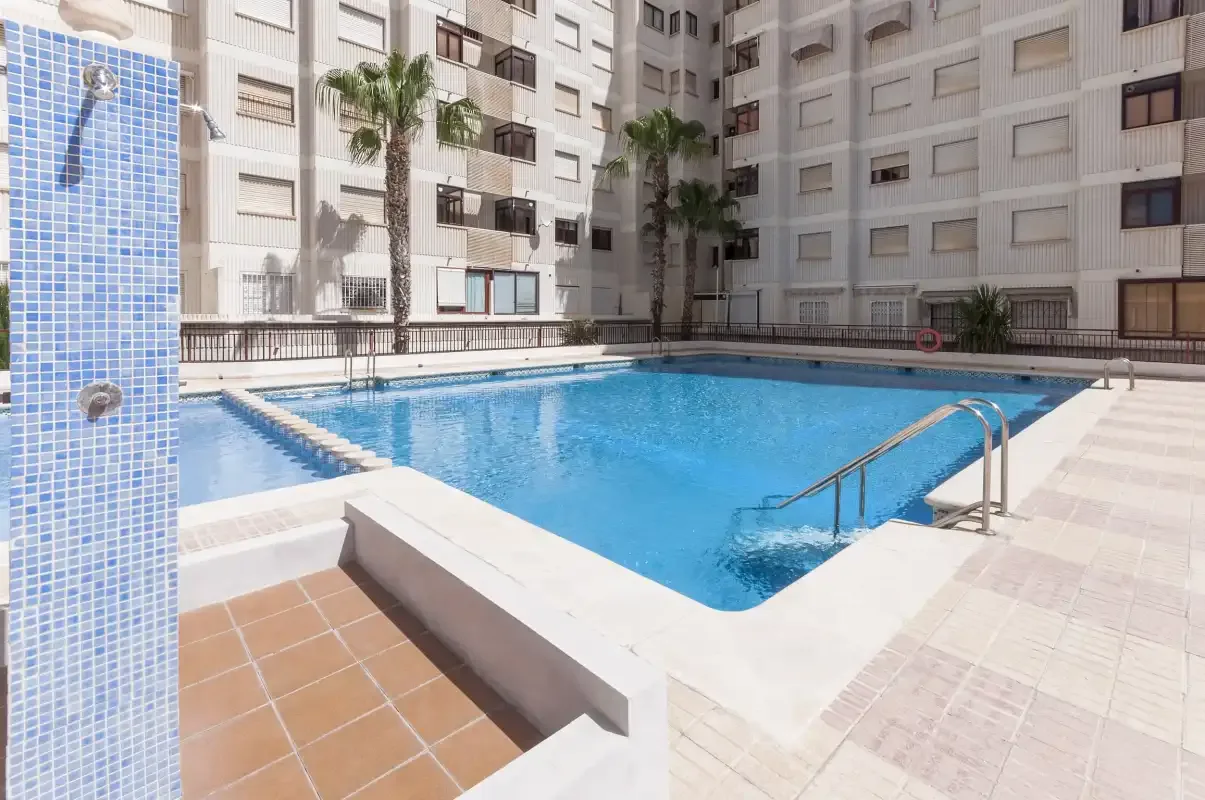 An outdoor swimming pool sits in a paved courtyard surrounded by apartment buildings.