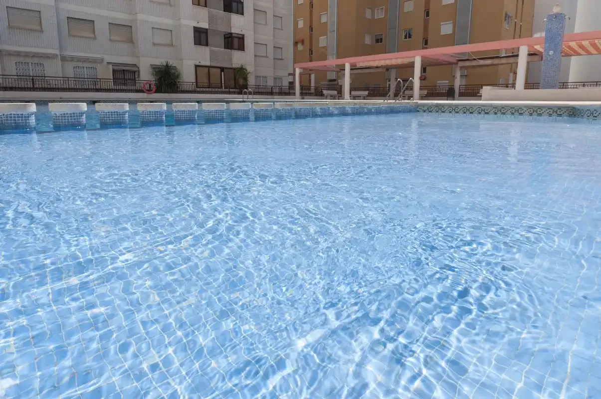 An outdoor swimming pool sits among apartment buildings and a covered seating area.