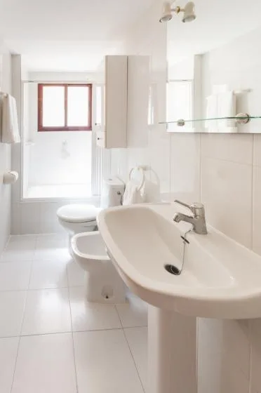 A bright bathroom with a sink, toilet, and window.