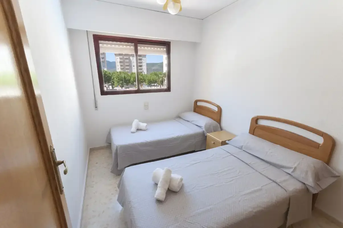A bedroom with two beds and a window overlooking greenery.