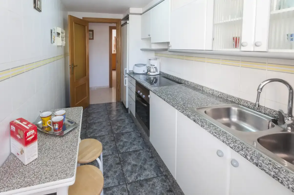 A tiled kitchen with a long countertop, sink, and upper cabinets.