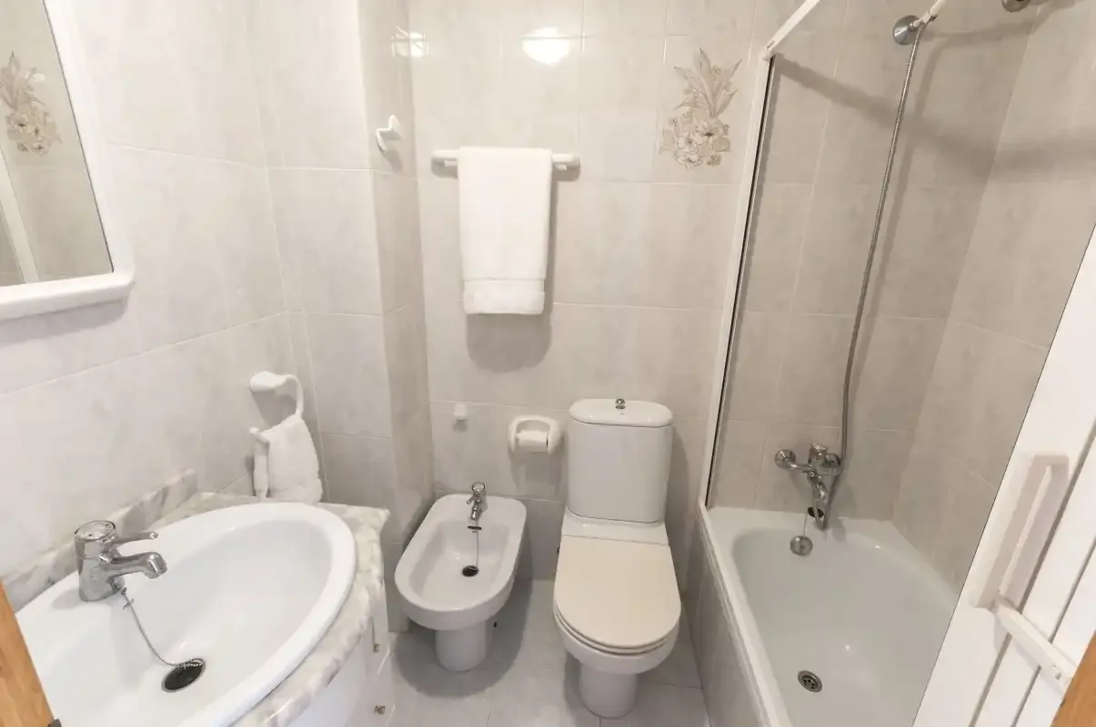 A tiled bathroom with a bathtub, sink, bidet, and toilet.