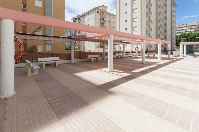 An outdoor paved terrace has shaded seating beneath a pink canopy.