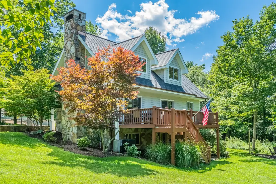A green house with a wooden deck sits among trees on a sunny day.