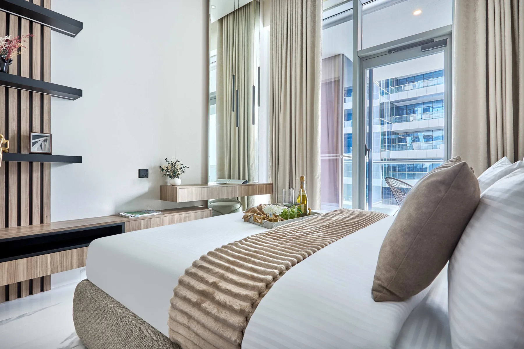 Un dormitorio con una cama bien tendida junto a ventanas altas y cortinas.
