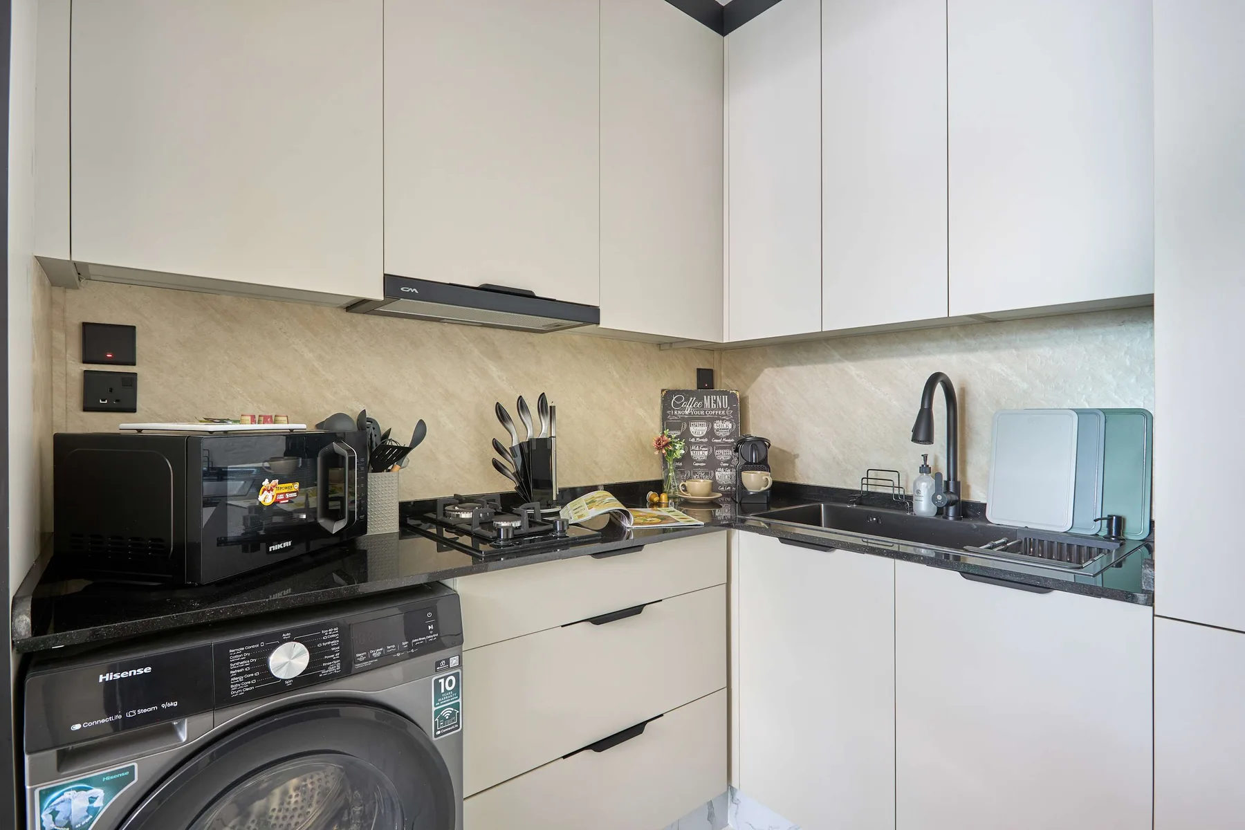 Una cocina compacta con gabinetes blancos, encimera negra y una placa de cocción.