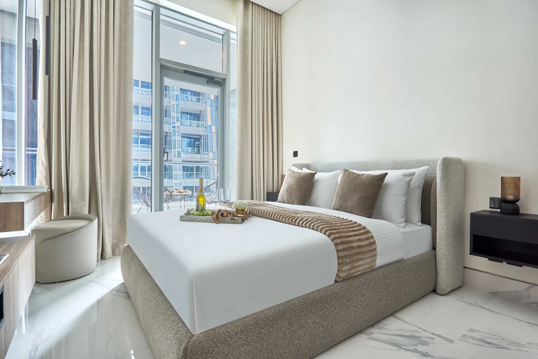 Un dormitorio luminoso con una cama junto a ventanas altas y cortinas.