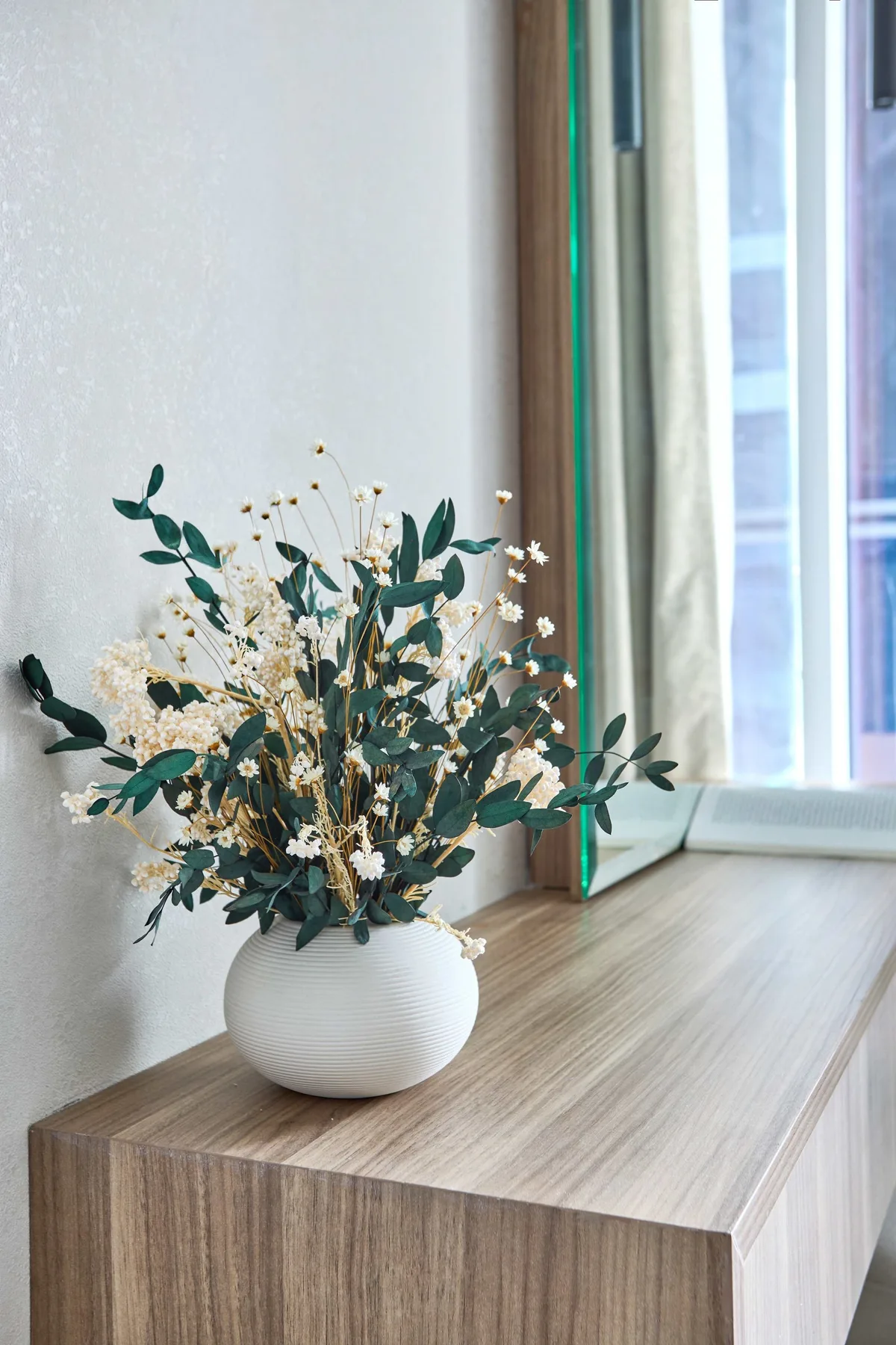 Un jarrón con flores está sobre una mesa de madera junto a una ventana.