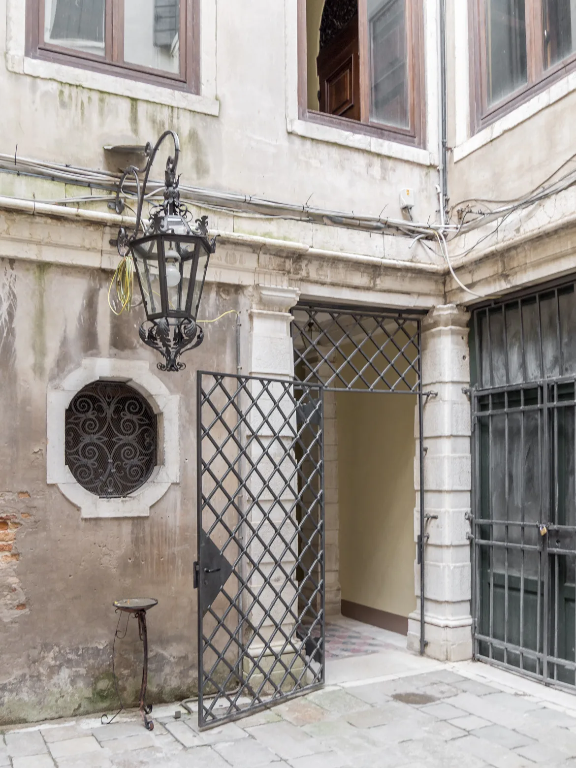 Una puerta metálica abierta da acceso a una entrada junto a una ventana enrejada.