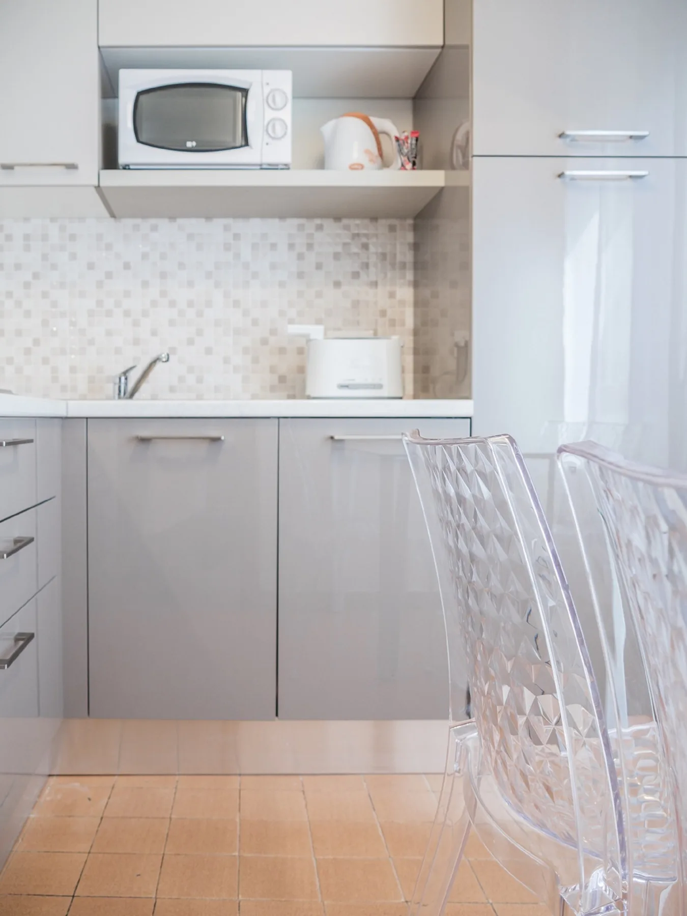 Una cocina luminosa con gabinetes claros, una encimera y asientos transparentes.