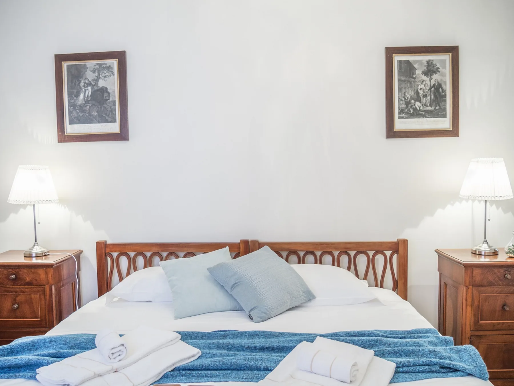 Un dormitorio con cama de madera, ropa de cama azul y mesitas a juego.