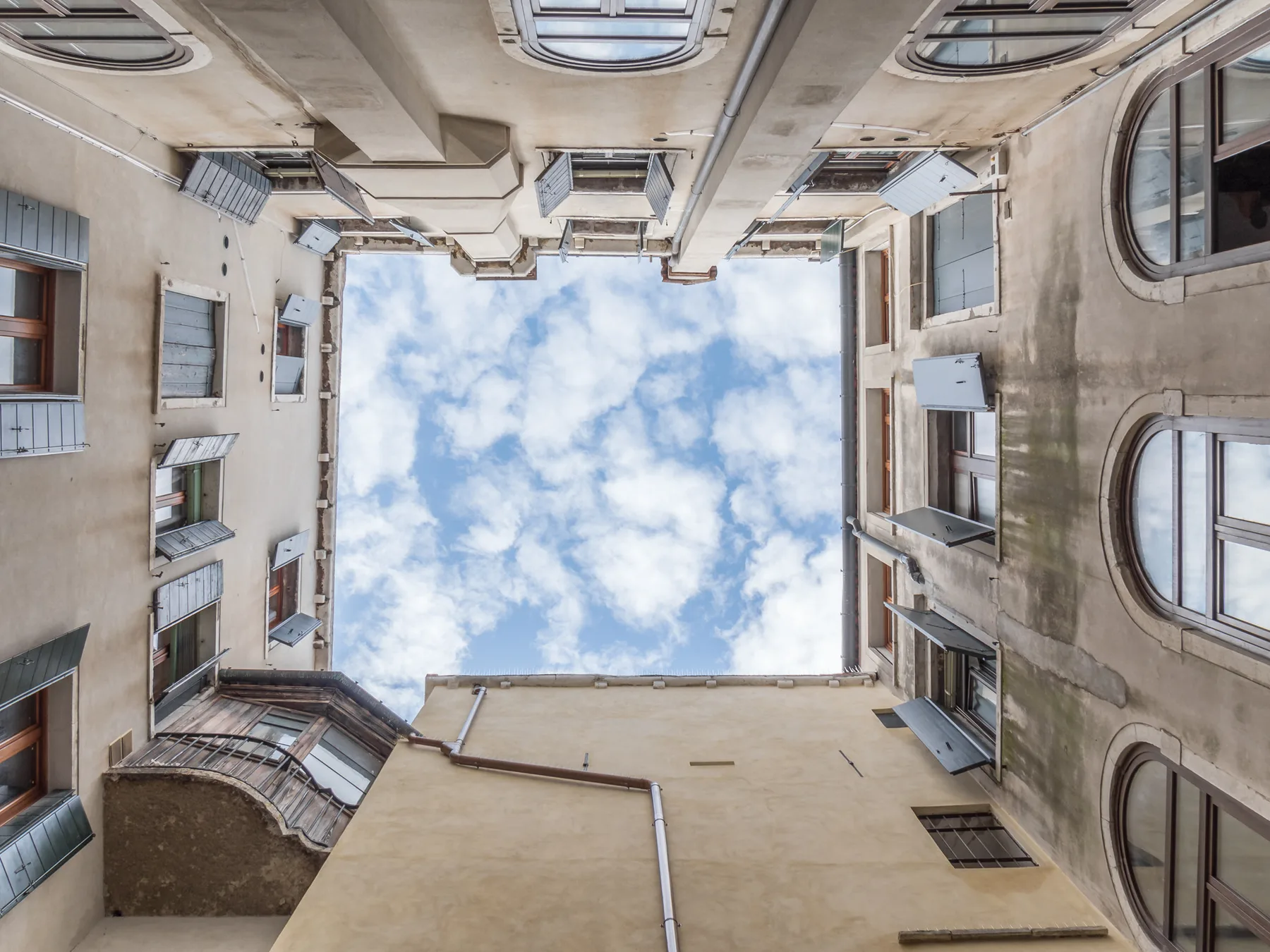 Vista hacia arriba de un patio, con fachadas de edificios alrededor de un tramo de cielo.